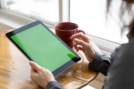 Close-up of woman hands holding chroma key green screen digital tablet in office or home.