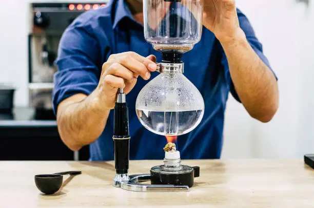 Photo of Professional coffee maker - Barista using coffee siphon brewing hot espresso at coffee shop.