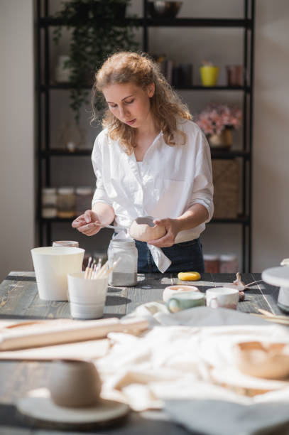 istock Female potter glazing raw unburned ceramic cup using brush. Earthenware mug putting colorant on pottery workshop 1297113193