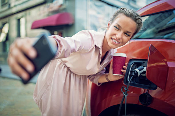 Young woman is taking selfie/making video call till charging her electric car Young woman is taking selfie/making video call till charging her electric car carsharing photos stock pictures, royalty-free photos & images
