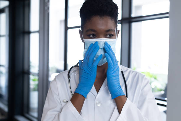 istock Mixed race female doctor standing putting a face mask on 1297116011