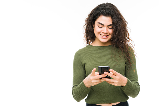 Hispanic woman typing and texting on her smart phone. Smiling young woman standing and sending a text message to a friend