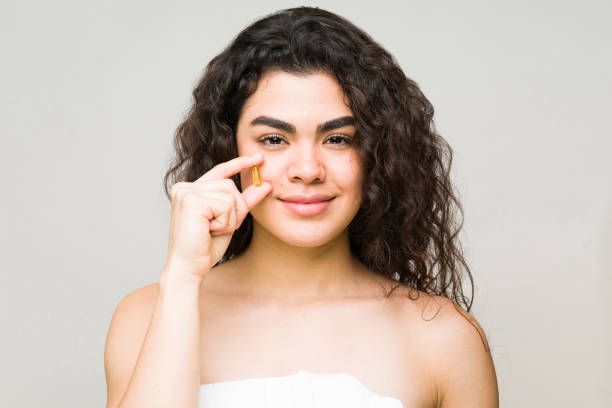 Female model holding a collagen in front of her face Good-looking hispanic woman about to take a collagen pill to maintain a youthful, wrinkle free skin and shiny long hair human collagen stock pictures, royalty-free photos & images