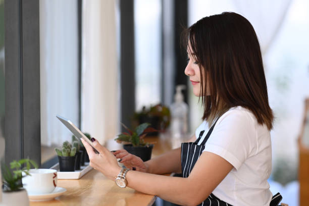 istock Female entrepreneur in an apron using a digital tablet while sitting near window in her coffee shop. 1297128253