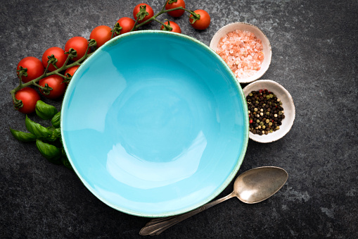 Empty blue ceramic bowl on black concrete background and ingredients. Top view, copy space, flat lay.
