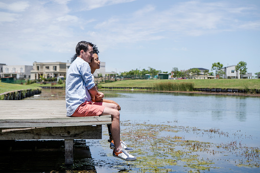 Thoughtful couple relaxing on pier by lake in garden