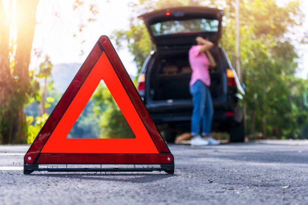 chiudere il segnale di arresto di emergenza rosso in piedi sulla strada. donna preoccupata e arrabbiata che cammina vicino alla sua auto rotta parlando al telefono con l'agente assicurativo. triangolo ravvicinato sulla strada laterale - ciglio della strada foto e immagini stock