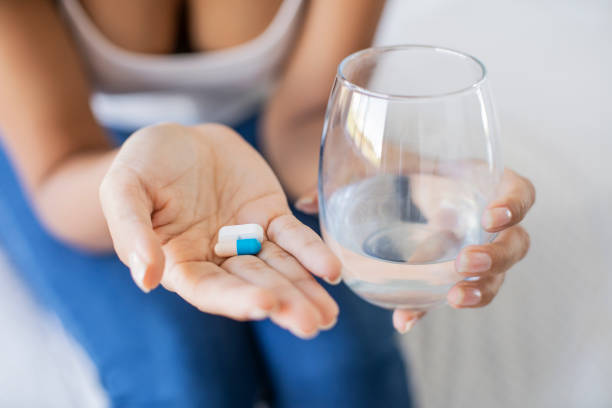 istock Young woman holding pills and water 1297131212