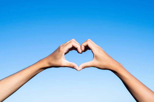 Close-up of young woman's hands making heart shape against sky