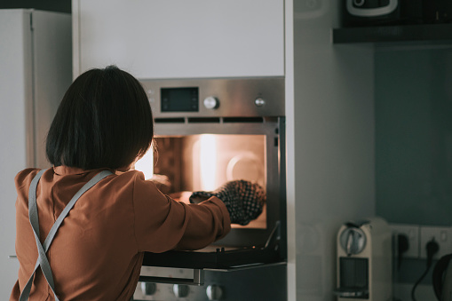 asian chinese young woman retrieving bakery item from electronic oven with protective glove