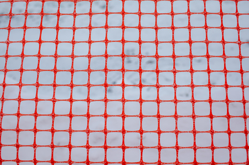 Plastic red safety net for construction site. Fencing repair work on the street. Construction grid on the background of winter snow