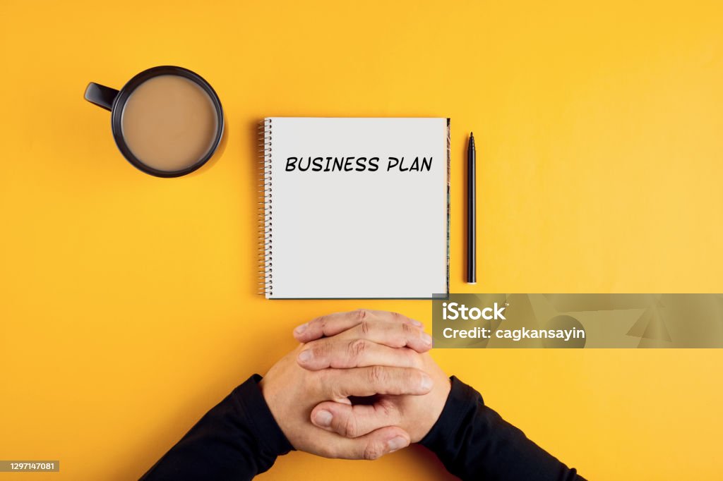 Hands of a businessman with spiral notebook with business plan ideas ready to be written in it. Hands of a businessman with spiral notebook with business plan ideas ready to be written in it. Yellow background with copy space. Business Plan Stock Photo