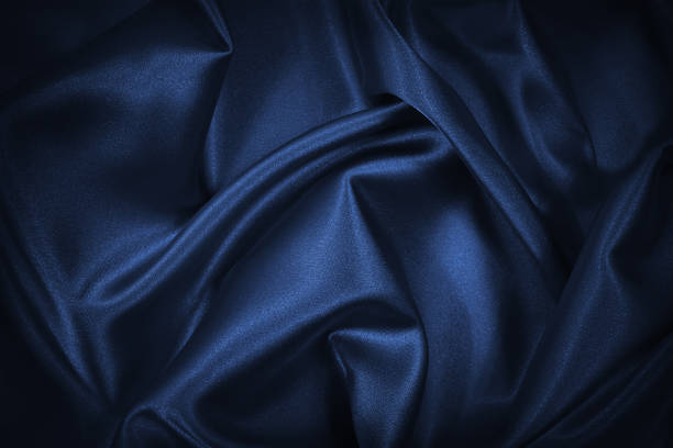 istock Abstract blue black background. Blue silk satin texture background. Beautiful soft wavy folds on shiny fabric. Dark elegant background for your design. 1297151634
