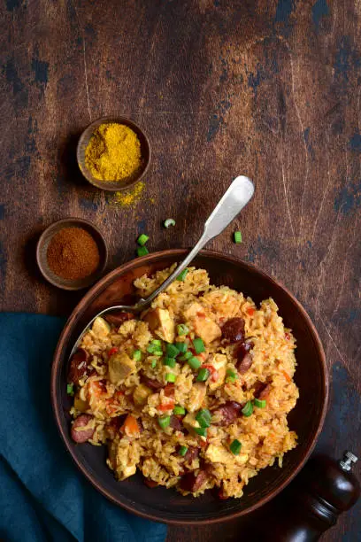 Jambalaya - spicy rice with tomatoes, meat and smoked sausage in a bowl on a dark wooden background. Top view with copy space.