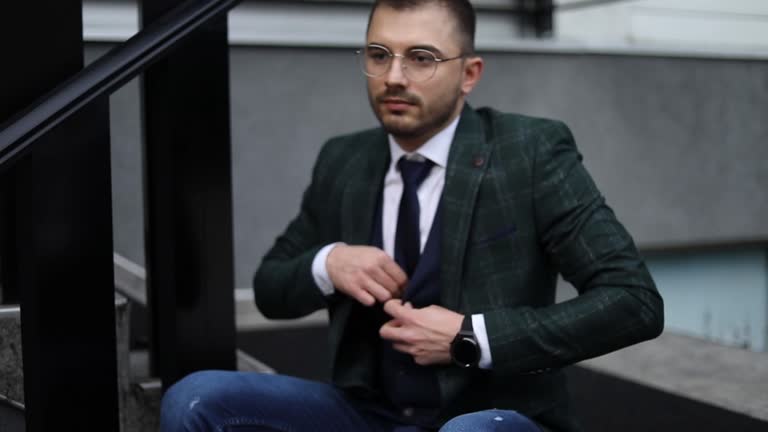 A businessman in front of an office building. A young businessman checks his suit and adjusts his tie in front of the office building