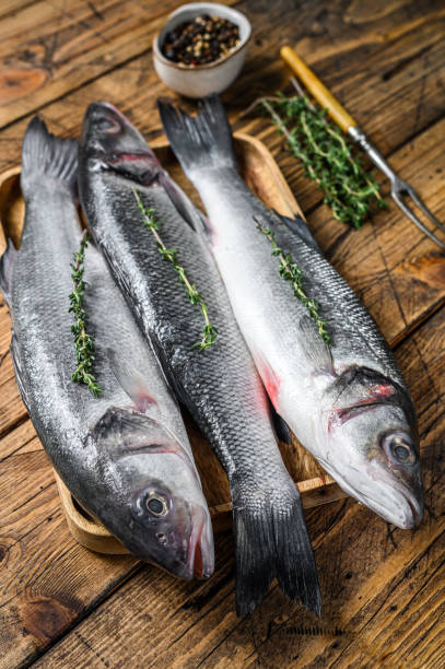 istock Raw seabass fish on a tray. wooden background. Top view 1297154879