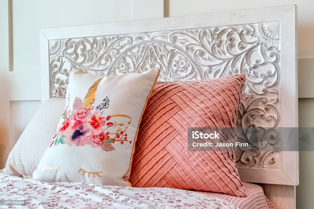 Fluffy pillows against decorative headboard of single bed against panelled wall Fluffy pillows against decorative headboard of single bed against panelled wall. Bedroom interior with an empty bed covered with pink and floral beddings. Architecture Stock Photo