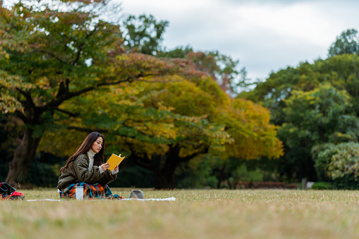 A young woman is sitting on grass and enjoying reading a book in nature.