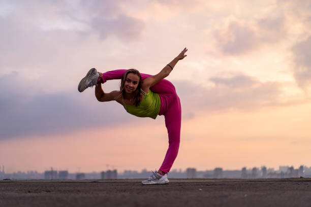 flexible frau tun split im freien auf dem dramatischen sonnenuntergang hintergrund. konzept von yoga, gesundem lebensstil und stretching - the splits flexibility yoga teenage girls stock-fotos und bilder