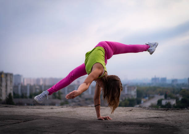 柔軟な女の子は、街並みの背景に分割して片手でバランスを保ちます。ポテンシャル、情熱、モチベーションの概念 - yoga city handstand control ストックフォトと画像