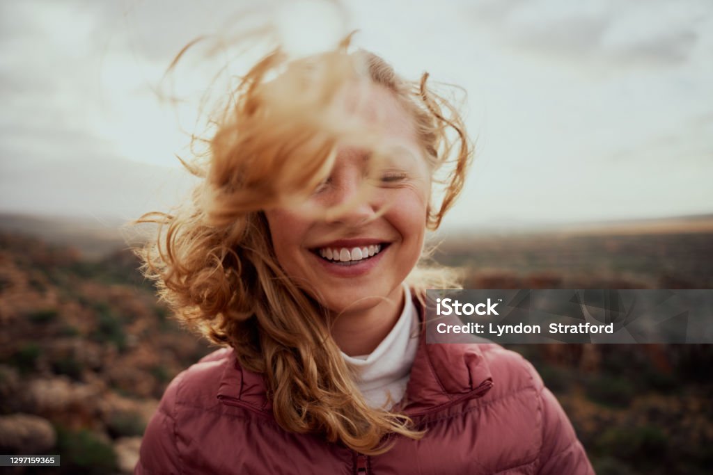 山に立つ風の強い日に飛ぶ髪で部分的に覆われた若い笑顔の女性の顔の肖像画 - 気楽な女性 - 女性のロイヤリティフリーストックフォト