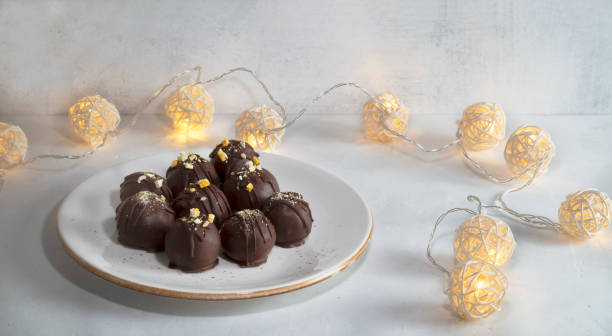 istock Chocolate truffles on a white plate. Grey background with yellow garland. 1297159707