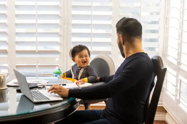 High quality stock photos of a man taking care of his children while teleconferencing with work from his home.