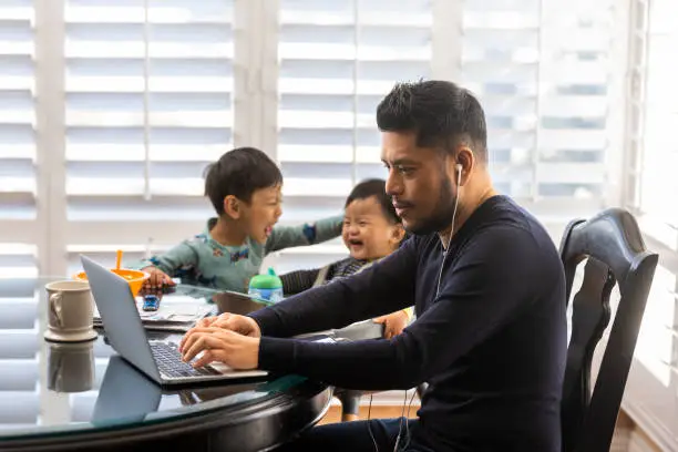 High quality stock photos of a man taking care of his children while teleconferencing with work from his home.