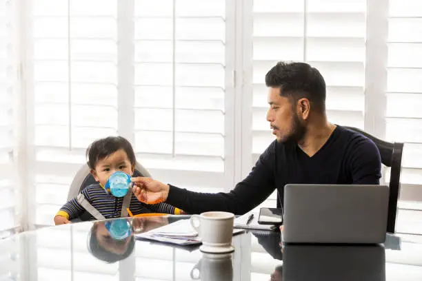 High quality stock photos of a man taking care of his children while teleconferencing with work from his home.