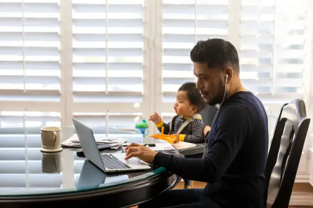 High quality stock photos of a man taking care of his children while teleconferencing with work from his home.