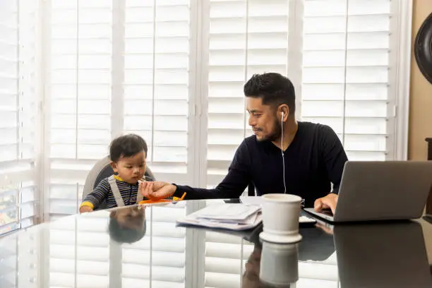 High quality stock photos of a man taking care of his children while teleconferencing with work from his home.