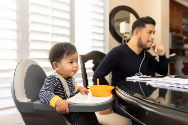 High quality stock photos of a man taking care of his children while teleconferencing with work from his home.