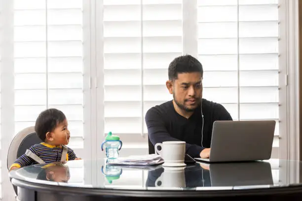 High quality stock photos of a man taking care of his children while teleconferencing with work from his home.