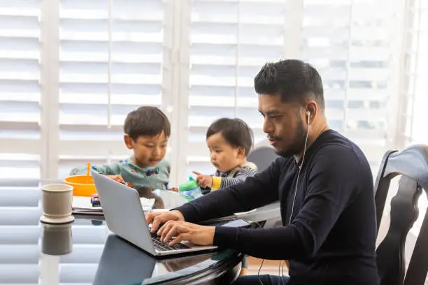 High quality stock photos of a man taking care of his children while teleconferencing with work from his home.