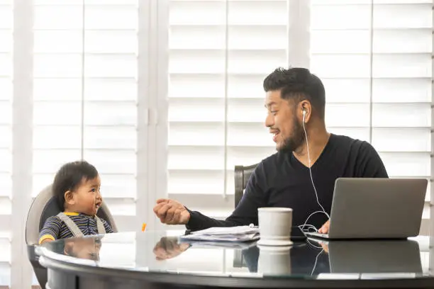 High quality stock photos of a man taking care of his children while teleconferencing with work from his home.
