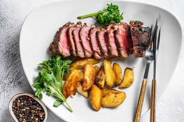 istock Sliced striploin steak with potato. White background. Top view 1297161346