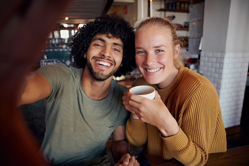 Portrait of smiling man with girlfriend taking selfie in modern cafe