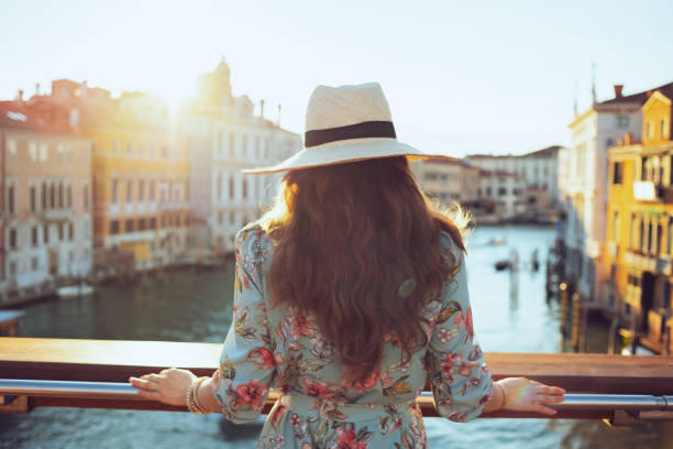 Seen from behind traveller woman in floral dress sightseeing Seen from behind modern traveller woman in floral dress with hat sightseeing on Accademia bridge in Venice, Italy. grand canal venice stock pictures, royalty-free photos & images