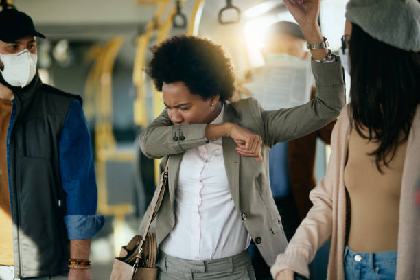 Black businesswoman sneezing into elbow while commuting to work by bus. African American businesswoman coughing into elbow while traveling by public transport. coughing stock pictures, royalty-free photos & images