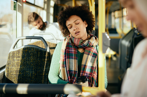 Exhausted African American woman taking a nap commuting by public transport..