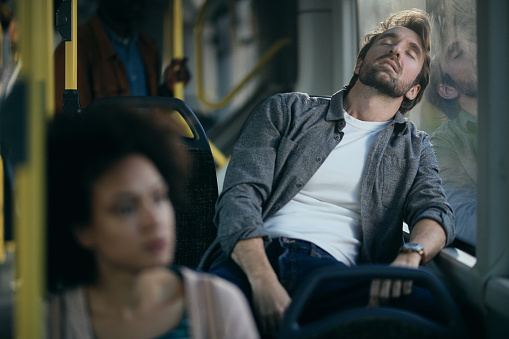 Exhausted mid adult man taking a nap while traveling by public transport.