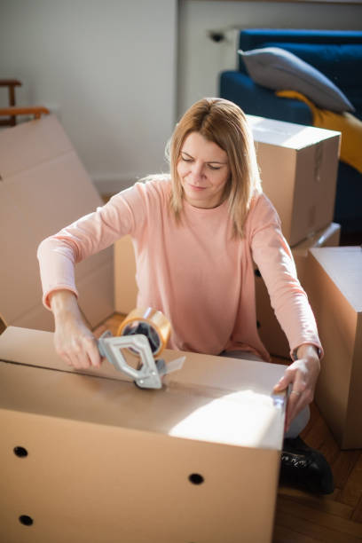 istock Woman using adhesive tape dispenser to close cardboard box 1297167336