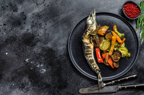 istock Baked whole icefish with grilled vegetables. Black background. Top view. Copy space 1297167598