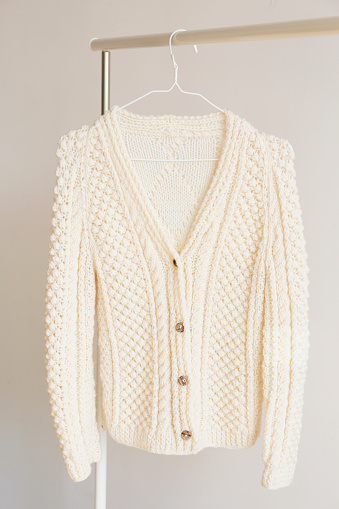 A single knitted warm pastel color sweater with original knitting patterns hanging on the rack, clearly visible texture. Stylish fall-winter season knitwear clothing. Close up, copy space