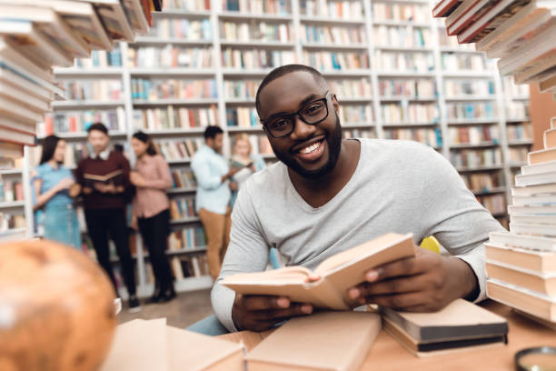 istock Ethnic african american guy surrounded by books in library. Student is reading book. 1297168556