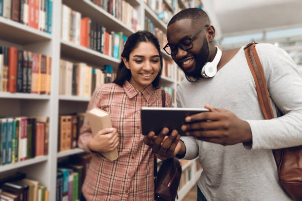 istock Ethnic indian mixed race girl and black guy in library. Students are using tablet. 1297168876