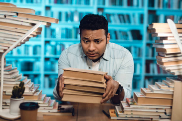 istock Ethnic indian mixed race guy surrounded by books in library. Student is holding books. 1297168951