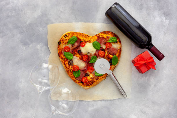istock Valentine's day table setting. Heart pizza with wine, glasses and gift box 1297169592
