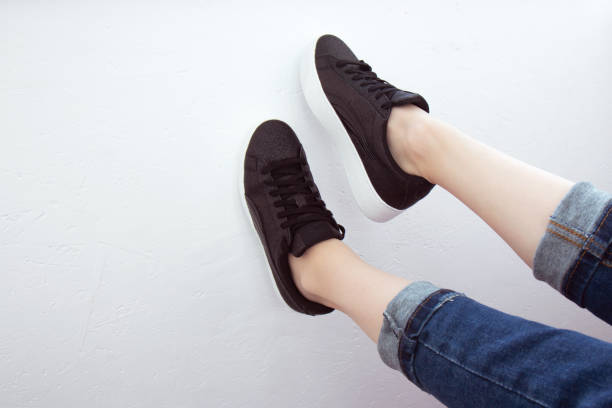 Female feet seen from above. Selfie for any use. Foot and legs in black sneakers and jeans. Foot raised on a white wall. With copy space. Feet outside