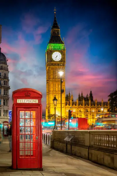 Red telephone booth in front of the illuminated Big Ben clocktower in London, United Kingdom, just after sunset with street traffic